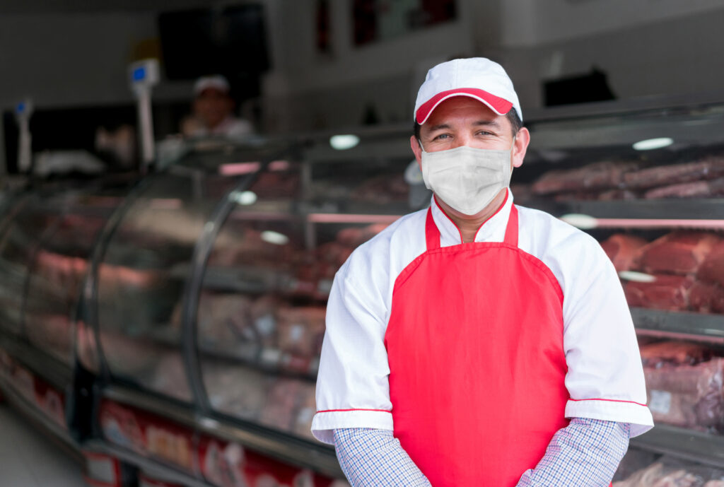 Worker standing in front of a deli in a uniform and mask